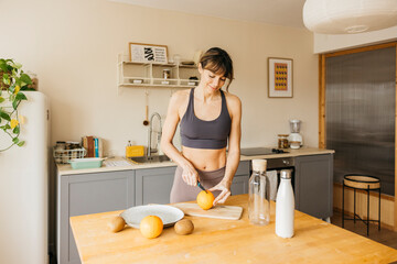 Woman in sportswear cutting fruit on a chopping board in a modern kitchen