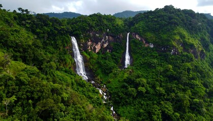 Aerial view of two waterfalls cascading down a lush green hillside. Verdant foliage surrounds the falls