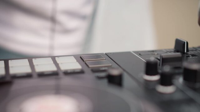 Closeup DJ controller black DJ hand mixing studio session focusing on tactile pads knobs jog wheel fader turntable male black DJ wearing white shirt manipulates pads and knobs to craft rhythm warm