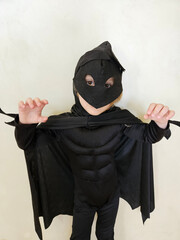 Young girl in a black super hero costume. He is wearing a black costume with mask and cape over shoulders