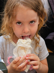 Girl is eating a banana split or ice cream. She is wearing a striped shirt. The banana split is covered in napkins