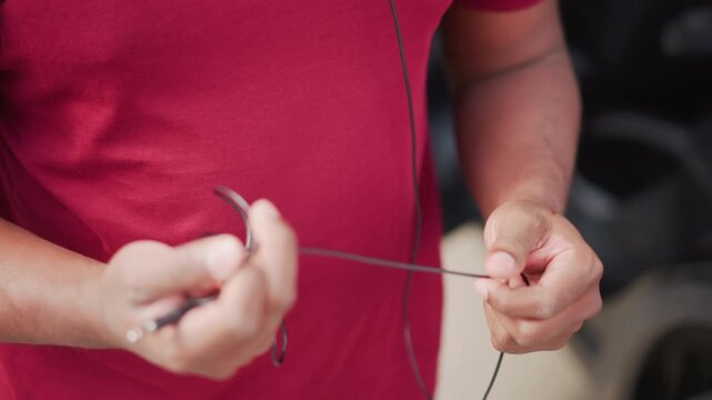 closeup hands Black musician untangling earbuds in red shirt on urban street, careful fingers working cable and plug, backpack visible, warm daylight, focused routine prepping set and checking audio