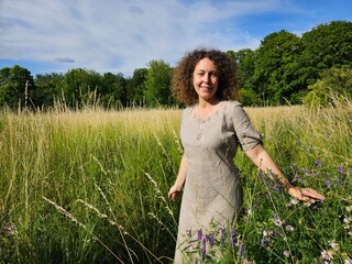 Woman is standing in a field of tall grass. She is wearing a dress and has her arms outstretched