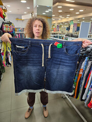 Woman is holding up a pair of blue jeans of giant size. The jeans are on display in a store
