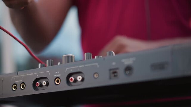 black DJ cable connection at mixer, closeup hands threading red RCA into input, adjusting gain knob and testing signal, urban rooftop soundcheck with focused musician preparing live set