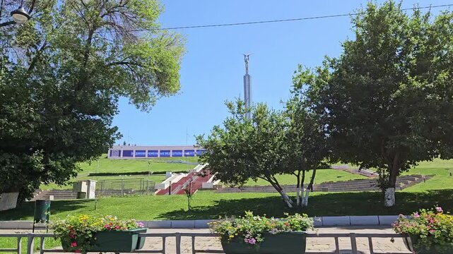 SAMARA - JUL 07, 2025: Group of people are walking on a path in a park near monument of Glory. There are three trees in the background and text on screen - payments, benefits and social guarantees