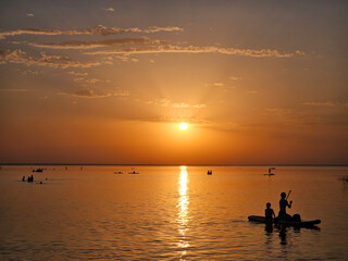 Group of people or Boy and a woman are paddling on a raft in the ocean. The sun is setting in the background