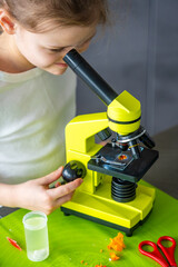 Close portrait of young girl looking through microscope during home science experiment. Focused scientific observation and early STEM education through hands on research activity.