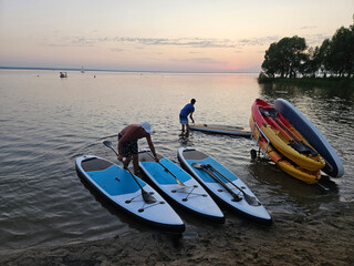 Man is getting ready to paddle a blue and white surfboard. There are other surfboards in the water, including a yellow one
