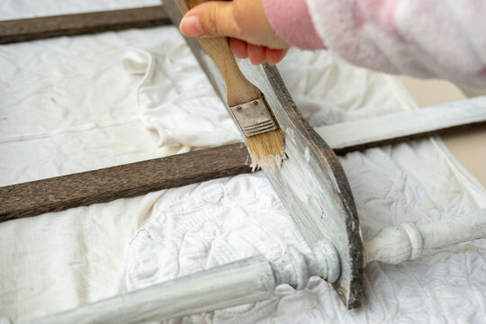 brush applying paint to old wooden furniture during furniture restoration, vintage bookcase restoration process, DIY home improvement and shabby chic style renovation project, hobby tool