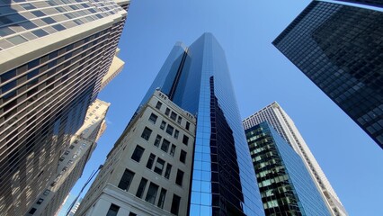 Fototapeta premium Looking up at towering skyscrapers reaching toward a clear blue sky, showcasing a blend of traditional and contemporary architecture defining an urban landscape