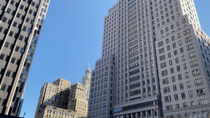 Modern and historical skyscrapers forming a dense urban canyon in the financial district of new york city, with office buildings reaching high into a bright blue sky