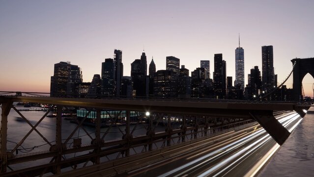 Brooklyn bridge structure framing a beautiful new york city skyline featuring one world trade center, showing light trails from vehicles moving over the bridge during twilight