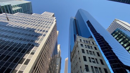 Obraz premium Towering glass and concrete skyscrapers ascend towards a clear blue sky, forming a modern urban landscape that symbolizes finance, business, development, and metropolitan living