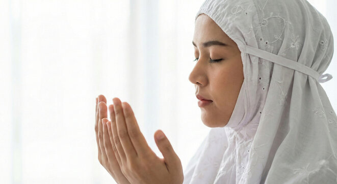 photo close up side profile of a woman in white mukena praying, hands raised in Dua