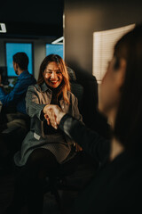 A businesswoman shakes hands with a colleague in a modern office, smiling during a light moment. Two coworkers seal a friendly agreement in a busy, contemporary workspace.