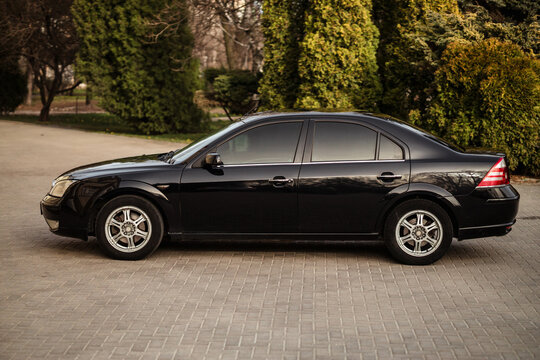 A horizontal shot of a black Ford Mondeo 2005 parked near a park