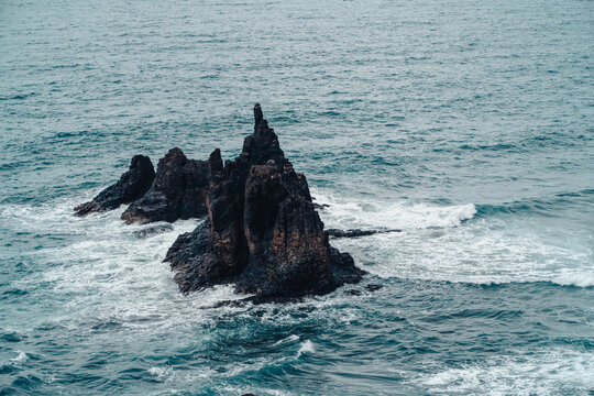 A dark rocks amist stromy wavy ocean in a cloudy weather.