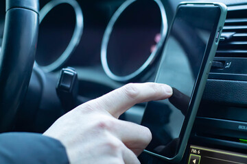 A close-up of a hand pressing a phone, the phone is attached to the car's dashboard. The dashboard features green-lit controls and buttons.