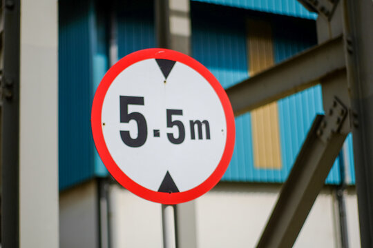 A Round White Height Restriction Sign Showing 5 5m Against a Blurred Industrial Background