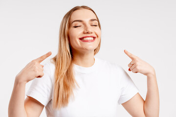 Happy young woman pointing teeth, presenting healthy smile on white background
