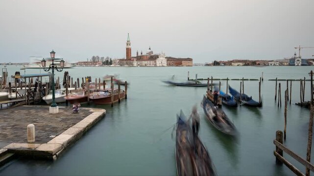 Timelapse of gondolas in Venice with tourists walking on the pier and San Giorgio Maggiore island and church on an overcast day