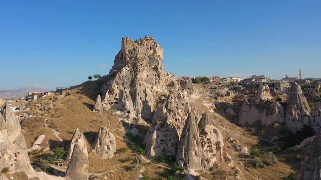 Aerial view of Uchisar Fortress and the surrounding town in Cappadocia, Turkey, bathed in warm sunset light under clear skies, showing the region's iconic rock formations.