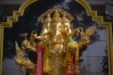 A statue of the three-headed Ganesha is placed outdoors for Buddhists and tourists to worship at Wat Pariwat Ratchasongkhram temple in Bangkok capital city in Thailand.