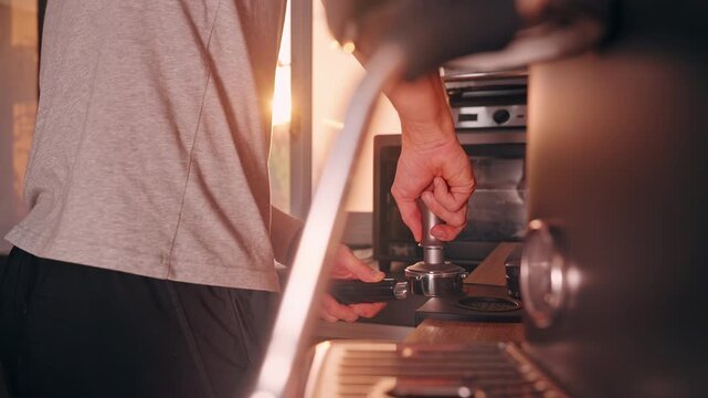 Man tamping Ground Coffee in Portafilter during Coffee Brewing in modern kitchen with Warm Light, Slow Motion close view of firm hand pressure near espresso machine