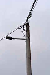 Low angle shot of a concrete utility pole equipped with a street lamp and numerous electrical wires against a flat grey overcast sky