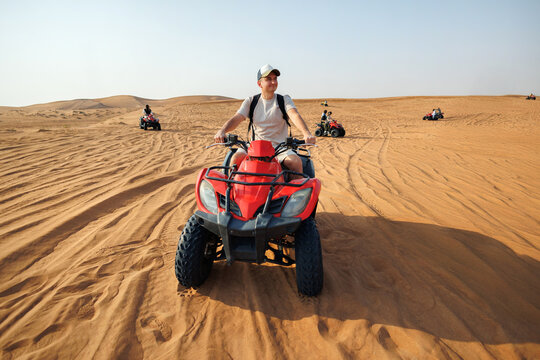 A man driving a red quad bike on sandy desert dunes. Extreme sports leisure activity for tourism.