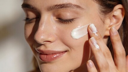 Woman applying moisturizer to face with closed eyes and gentle smile