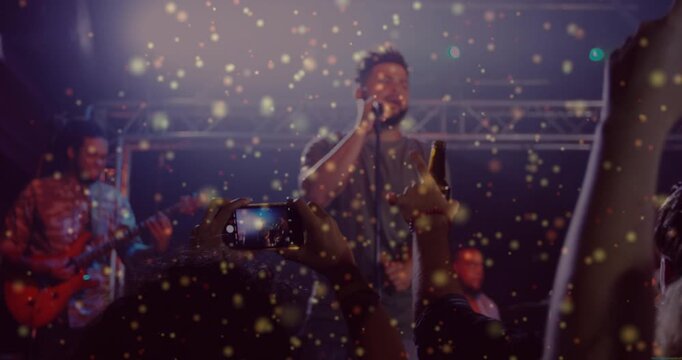 Singer starting song stage, crowd raising phones, recording as golden glitter drifting over phones