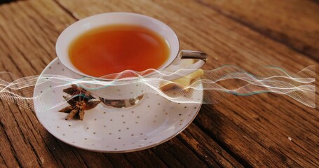 Sitting porcelain teacup, gold-dot saucer holding tea on wood table, star anise, spoon, lemon, wave