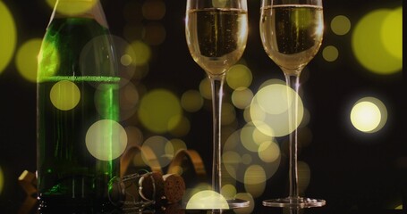 Showing two flutes fizzing on black reflective table with green bottle, popped cork, bokeh lights