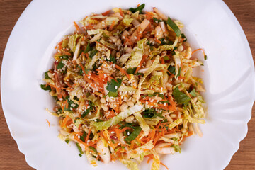 A ready-made salad of cabbage, carrots and apples with nuts and sauce on a white plate on a wooden table.