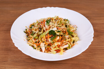 A ready-made salad of cabbage, carrots and apples with nuts and sauce on a white plate on a wooden table.