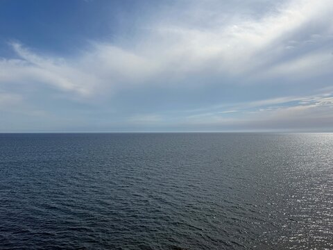 Calm ocean, open sea, blue sky, clouds, horizon.