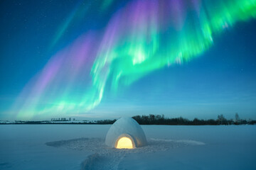 Obraz premium Winter night landscape with illuminated igloo in snow-covered field, northern lights, aurora borealis, polar lights. Christmas postcard background
