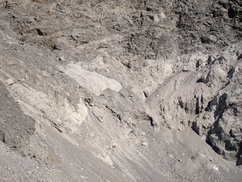 A detailed view of a steep limestone embankment within a quarry. The image shows layers of light grey crushed stone, mineral dust, and rugged rock formations from active mining.