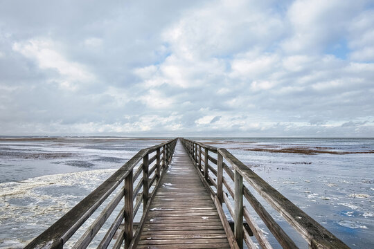 Diminishing Perspective view of a long wooden boardwalk stretching to the horizon across icy Cape Cod Bay at Grays Beach in Yarmouth, Massachusetts.