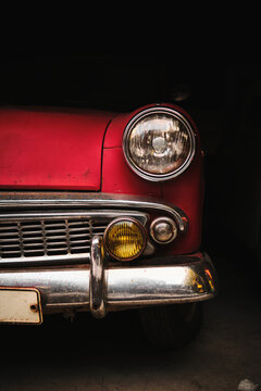 Close-up detail of red vintage car headlight with chrome bumper. Retro automotive design with dark background.