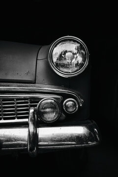 Front detail of gray vintage car with round headlight. Retro automobile parked indoors with moody lighting.