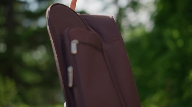 Guitar case scene. Closeup of musician with guitar case. Hands zipping brown guitar case in forest setting. Calm scene of musician preparing instrument with forest backdrop and sunlight