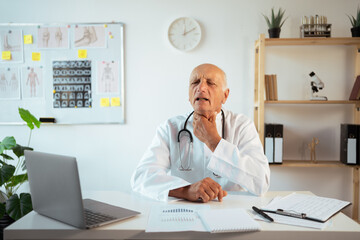 Senior male doctor suffering throat sore and flu on workspace sitting in modern medical clinic
