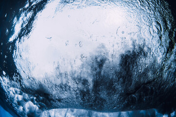 Inside a breaking ocean wave from underwater perspective, dramatic blue tunnel with light, motion and raw power.