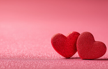 Fototapeta premium two red hearts on a pink glittery background with copy space for a valentine's day celebration, a love concept. 