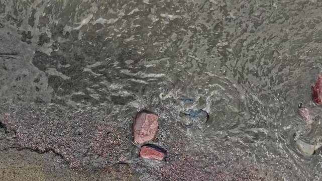 Aerial still top-down footage of T&uuml;risalu coastline with wild sandy beach, scattered boulders, textured shoreline patterns, and gentle Baltic waves. Natural tones, calm weather, and detailed coastal g