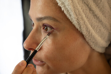 Woman blending eyeshadow with a makeup brush on her face.
Beauty and skincare routine concept. Professional makeup application, cosmetics, self-care, and personal grooming. Close-up portrait.