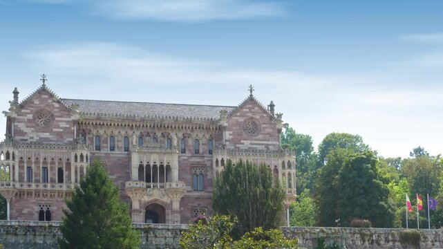 Ornate neogothic architecture of the Sobrellano Palace, a magnificent historic landmark in Comillas, Cantabria, surrounded by lush green trees against a beautiful blue sky on a sunny day